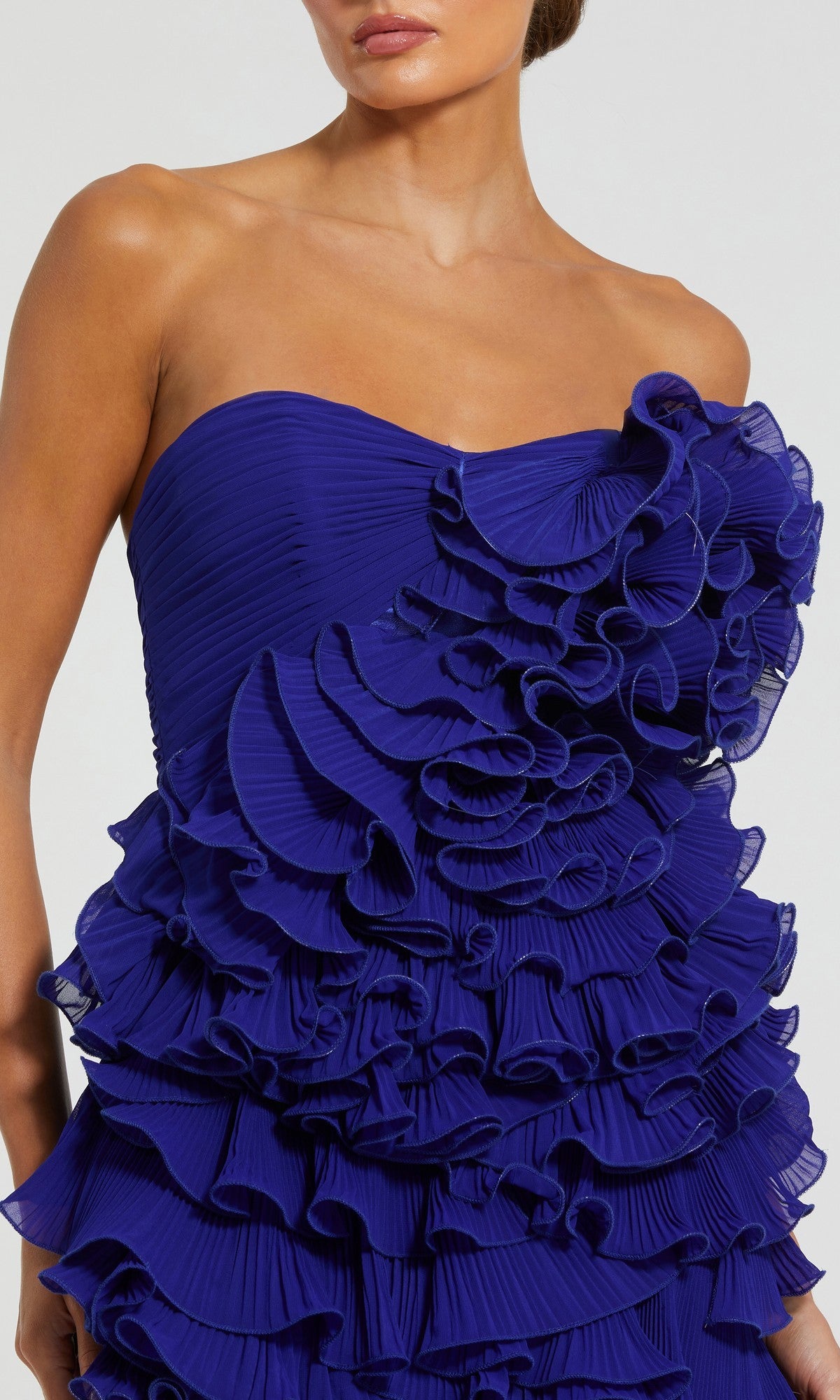 A woman wears the Mac Duggal 11766 short party dress, a strapless design in vibrant royal blue with multiple layers of pleated ruffles for the ultimate tiered ruffle party look.